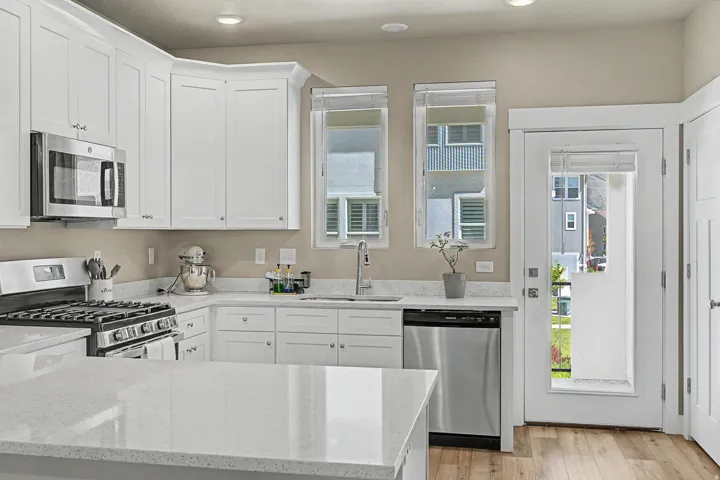 Modern kitchen featuring white shaker cabinetry, stainless steel appliances, light-toned countertops, and wood-finish flooring
