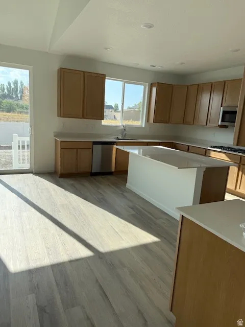 Kitchen featuring wood cabinetry, stainless steel appliances, a center island with quartz countertop, and LVT flooring
