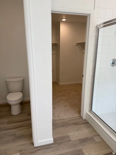 Primary ensuite bath. Walk-in shower with clear glass enclosure and subway tile surround, wood-finish flooring, and a separate water closet