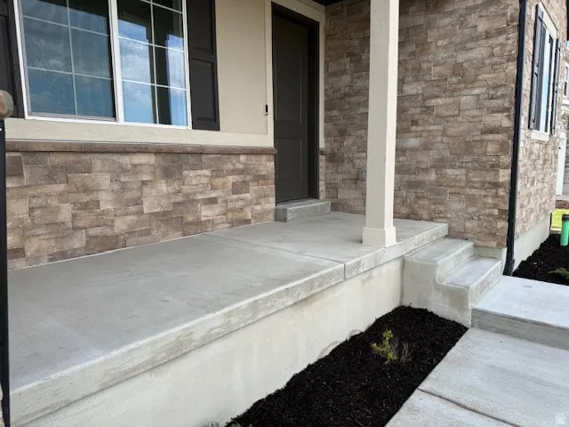 Stone siding accents a concrete porch with a white column, dark shutters, and a dark entry door
