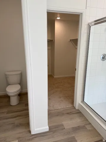 Primary ensuite bath. Walk-in shower with clear glass enclosure and subway tile surround, wood-finish flooring, and a separate water closet