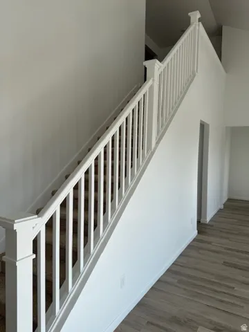 Carpeted staircase with white balusters, wood-finish flooring, and white walls