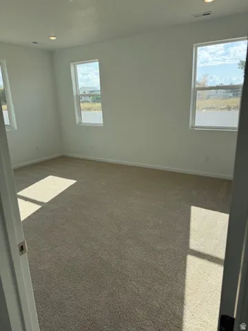 Neutral toned carpeting with recessed lighting and multiple windows