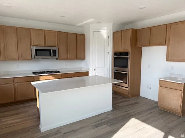 Kitchen featuring wood cabinetry, stainless steel appliances, a center island with quartz countertop, and LVT flooring