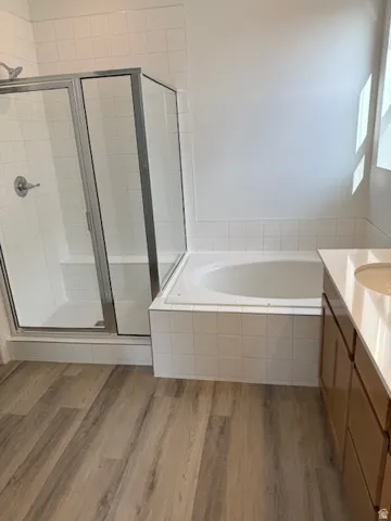 Primary Ensuite Bath with white tile shower and garden tub. Wood-finish flooring, white tiled shower with glass enclosure, built-in bathtub with tiled surround, and a vanity with an integrated sink and light wood cabinetry