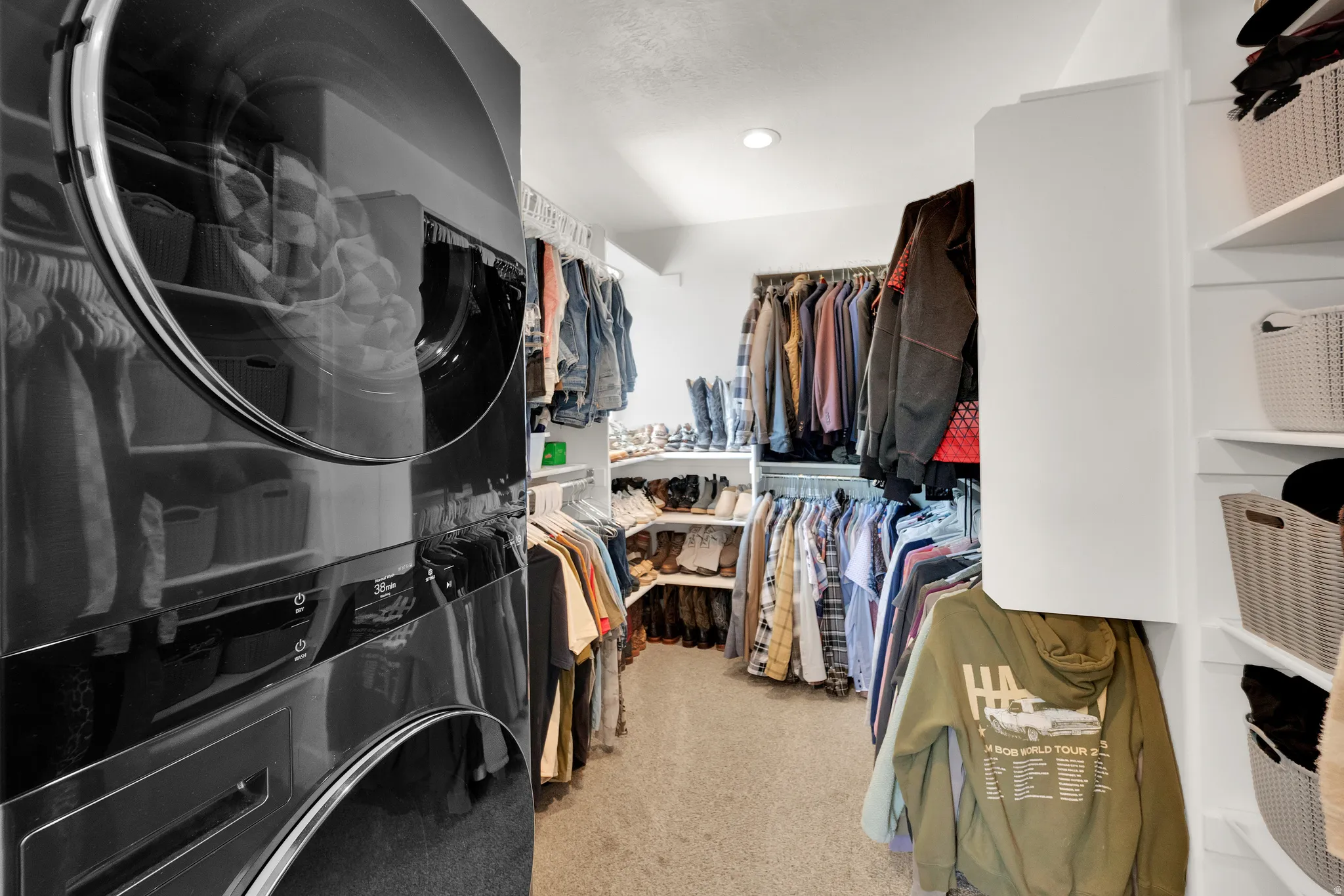 Primary walk in closet with dedicated laundry with stacked washer and dryer, integrated within a walk-in closet featuring extensive built-in shelving, hanging rods, and recessed lighting