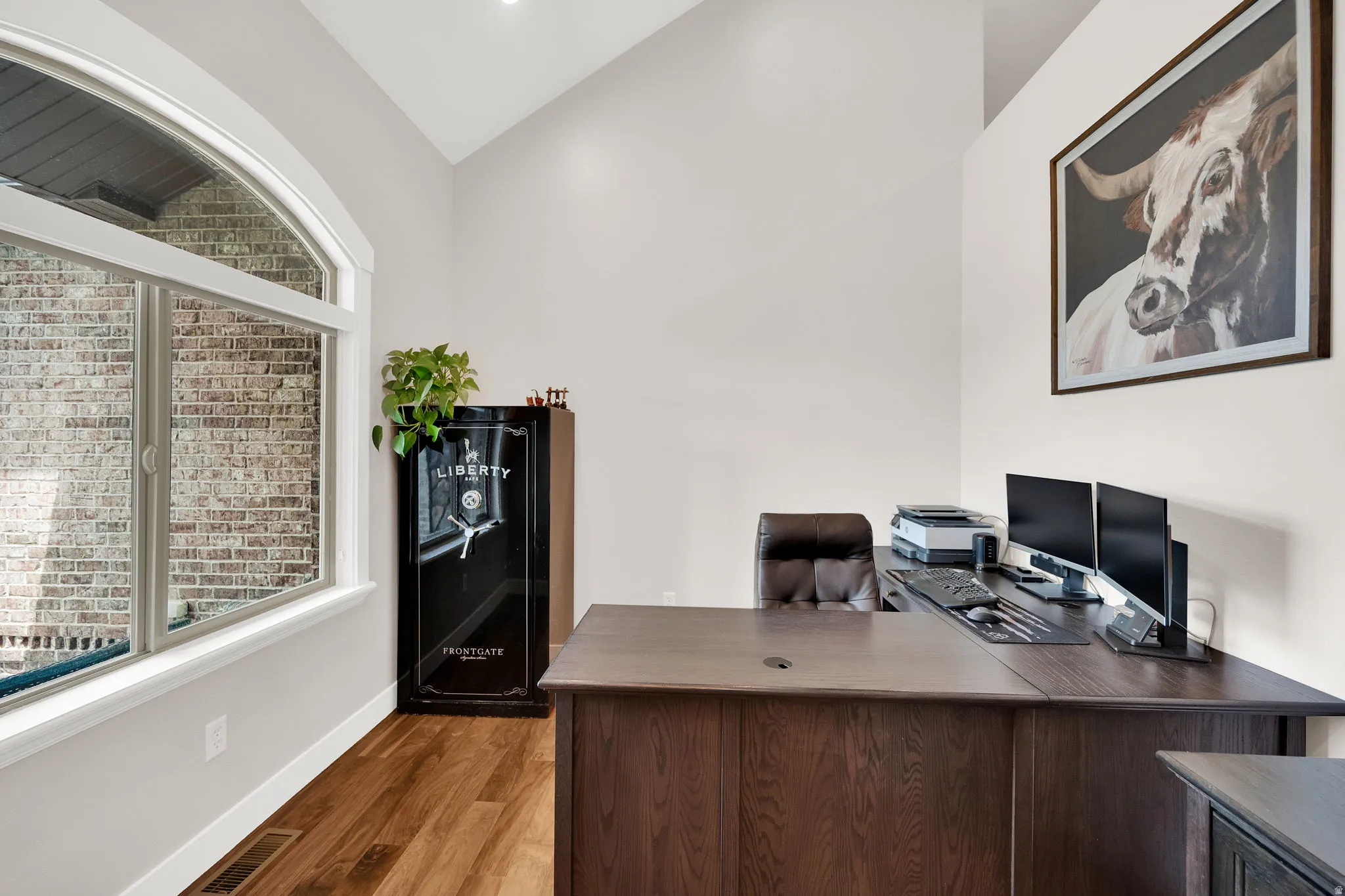 Vaulted ceiling office space featuring wood-finish flooring and an arched window