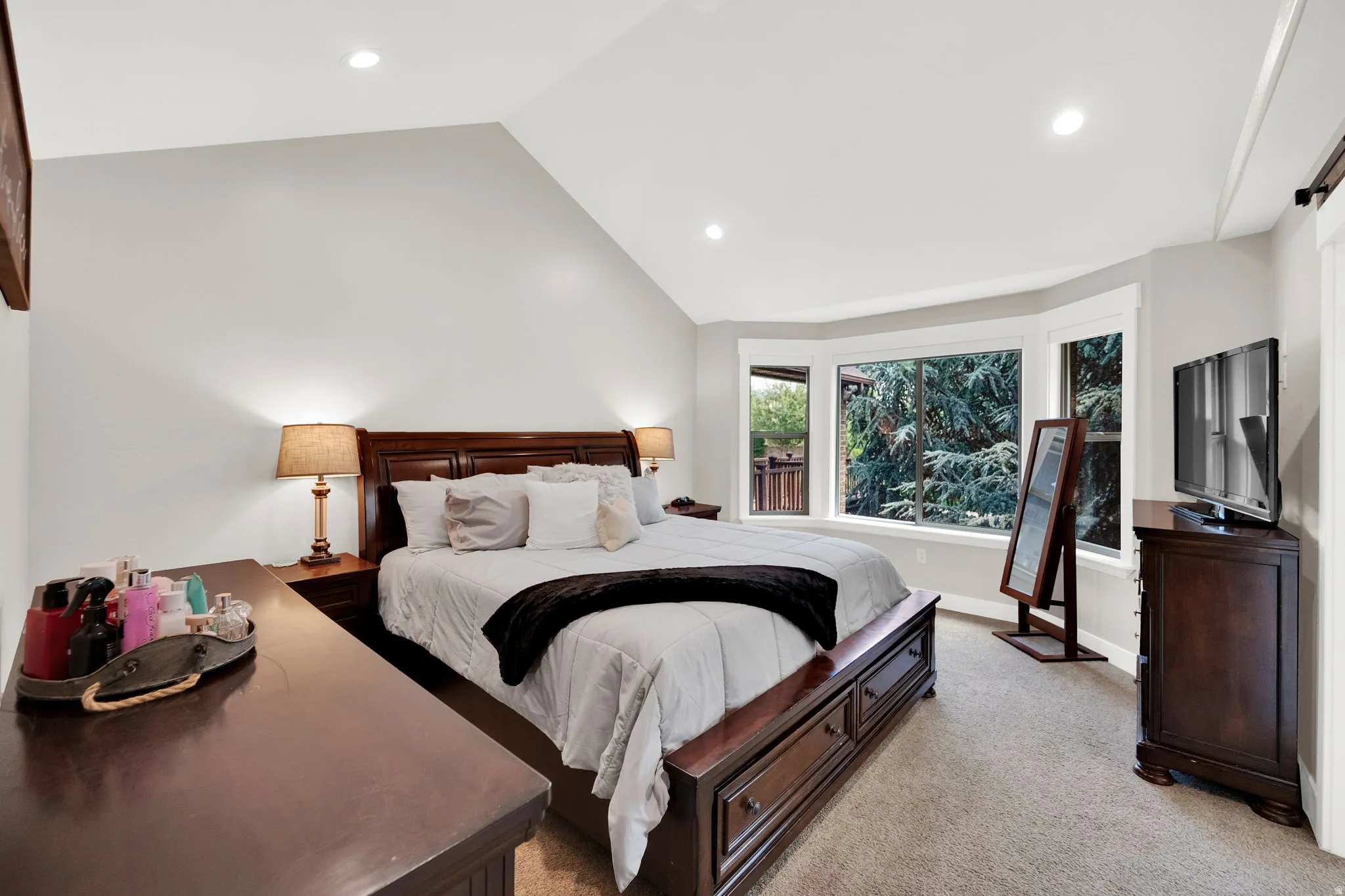 Primary suite featuring a vaulted ceiling with recessed lighting, bay windows with white trim, and light-colored carpeting