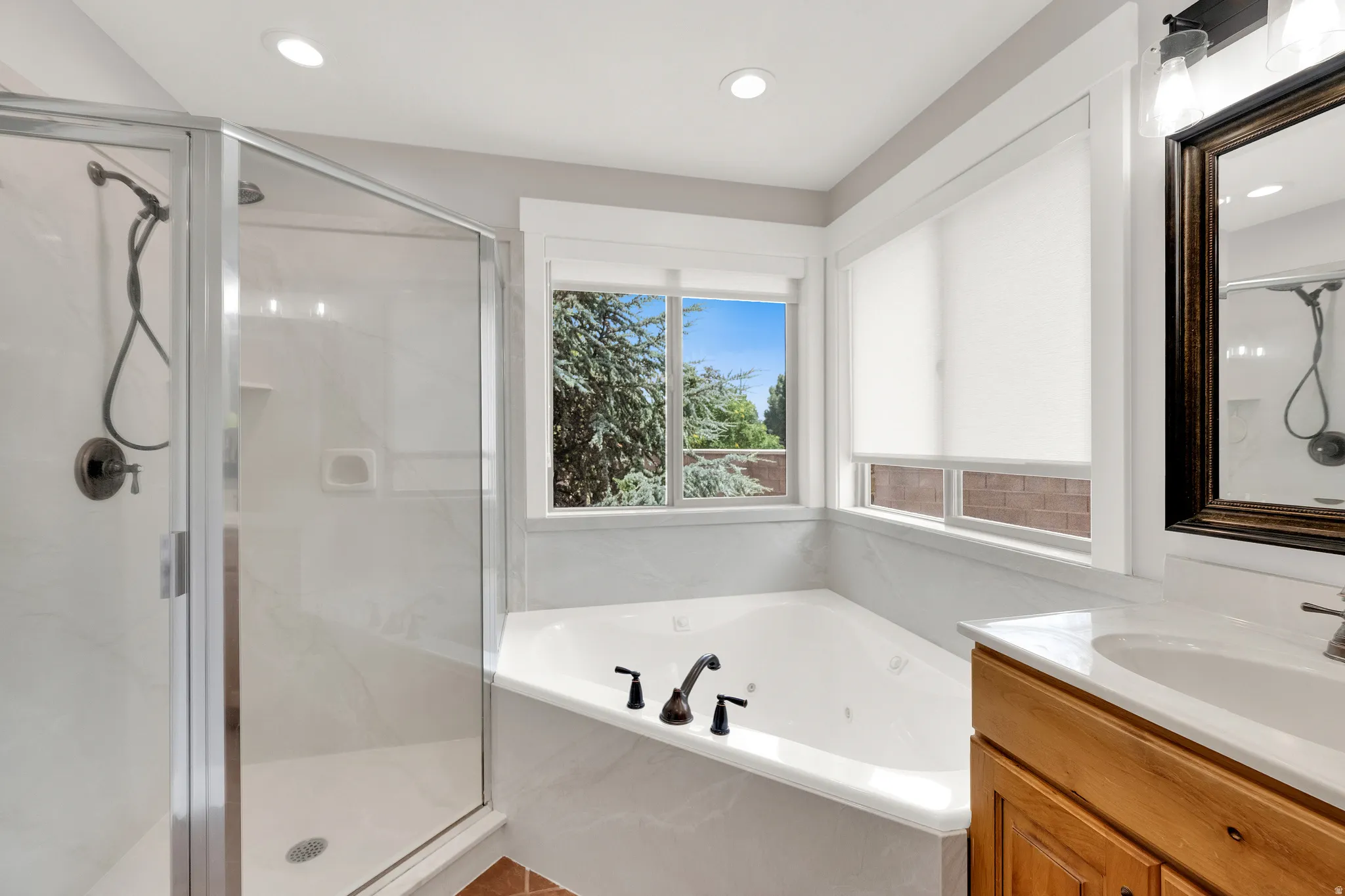 Primary Bathroom featuring a corner soaking tub with matte black fixtures, an adjacent walk-in shower with a glass enclosure, and a dual vanity with a white countertop.