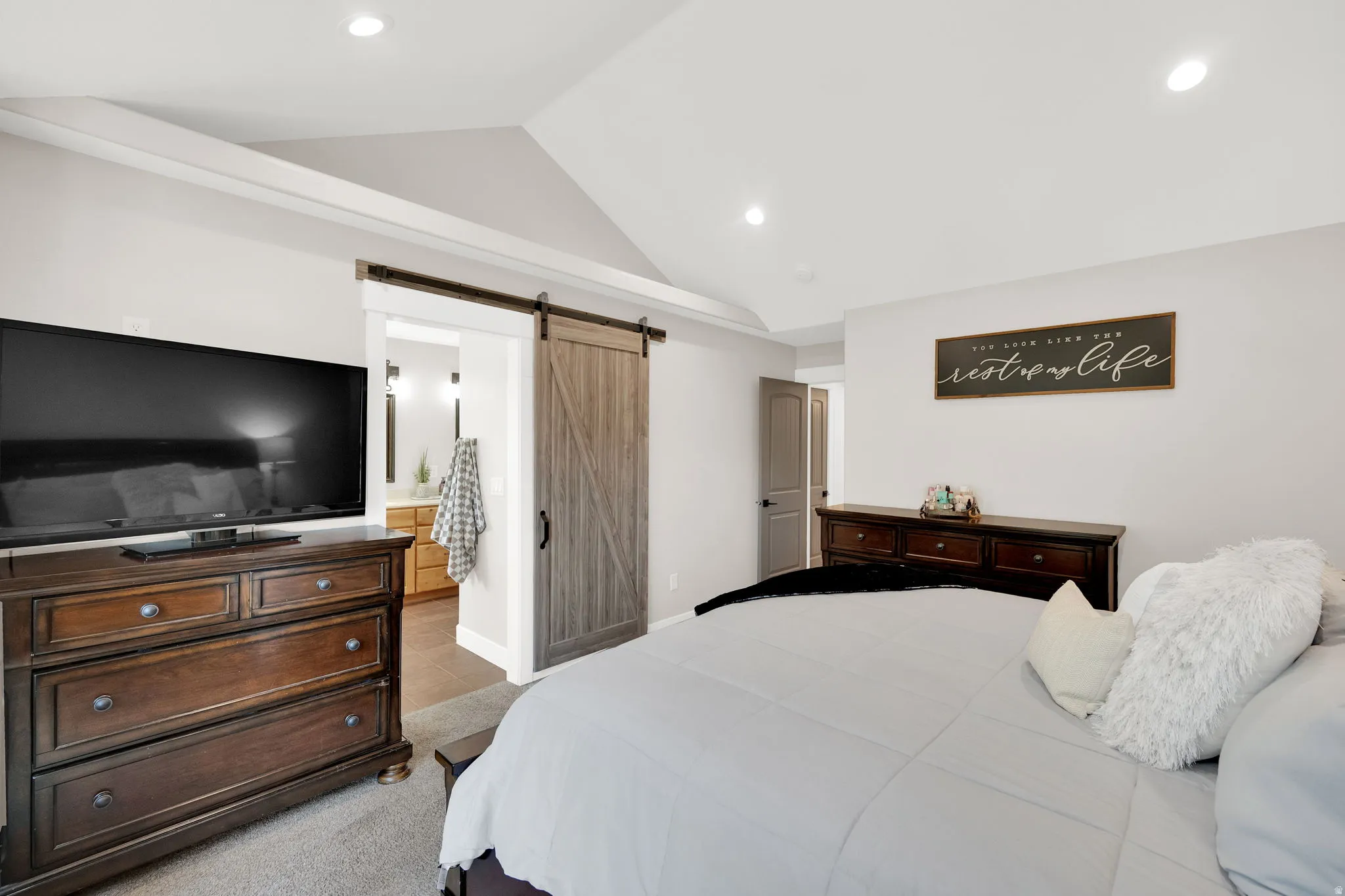 Spacious primary room featuring vaulted ceilings, recessed lighting, and barn door.