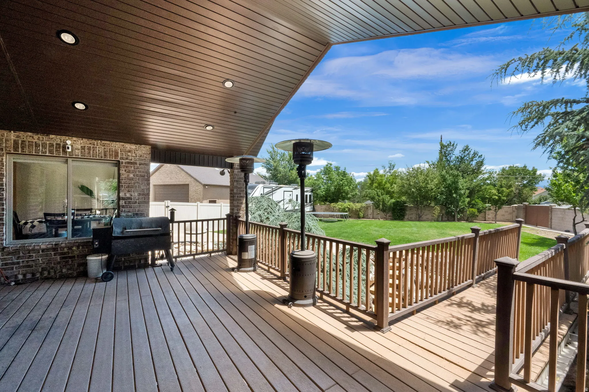 Spacious covered deck featuring wood-finish decking, dark wood railings, and recessed lighting