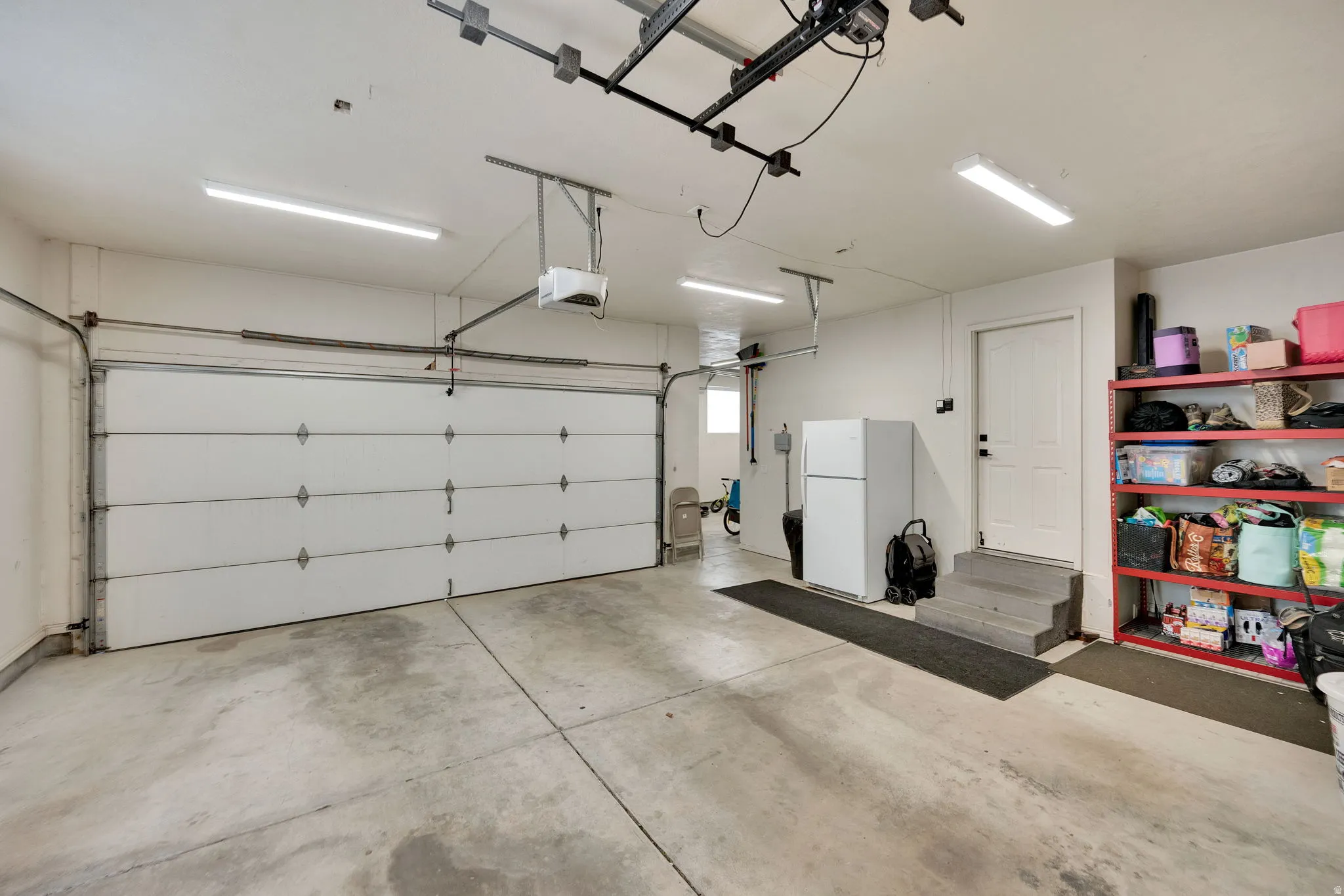 Spacious attached 2-car garage featuring a concrete floor, overhead lighting, and a white paneled garage door