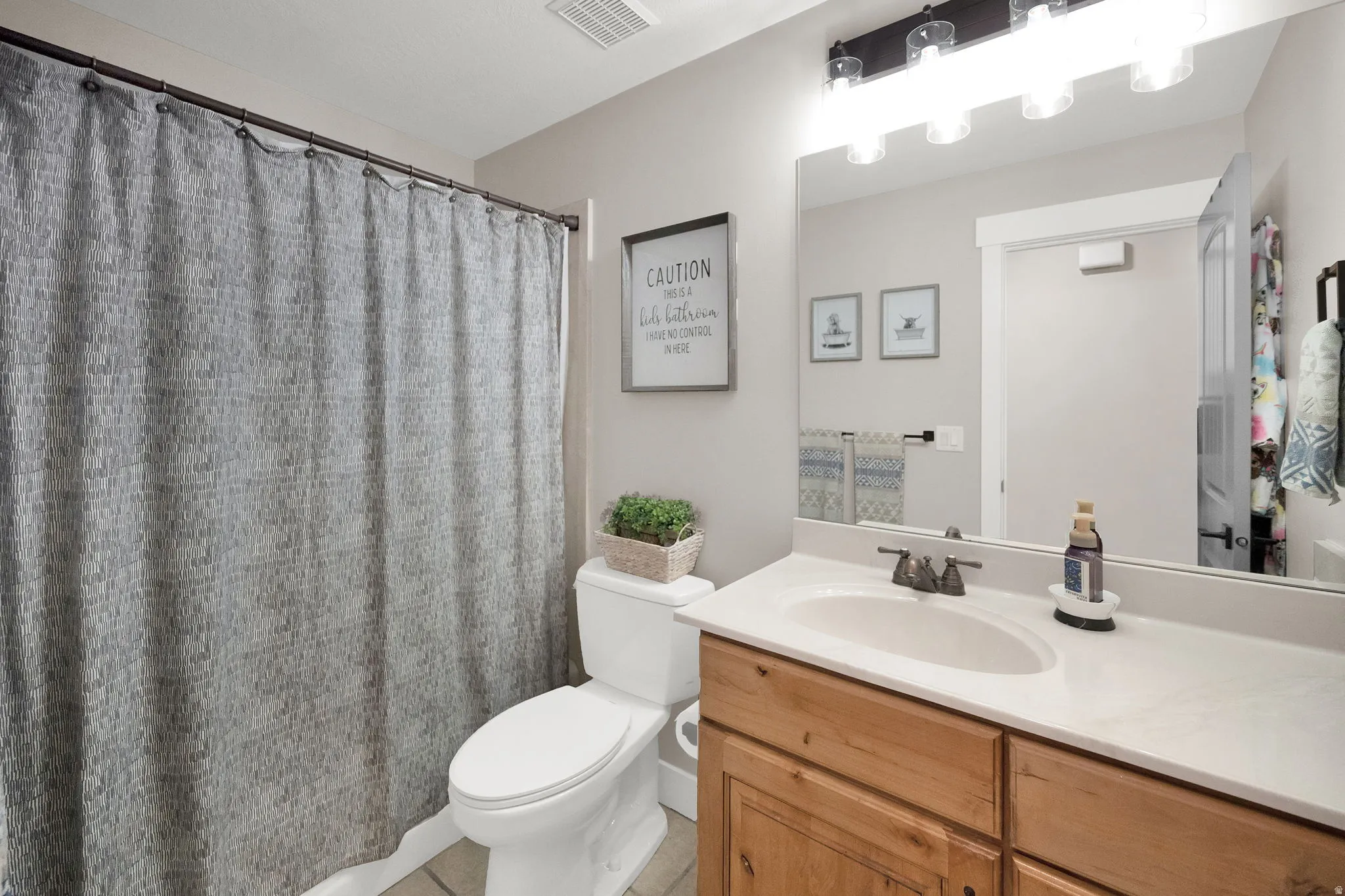 Bathroom featuring a wood-finish vanity with an integrated sink and light-toned countertop, an overhead mirror, and a multi-bulb vanity light fixture