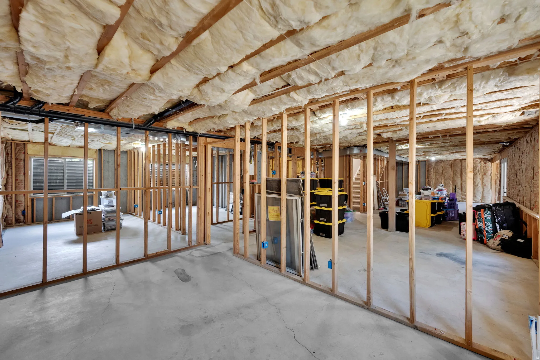 Unfinished lower level featuring exposed wood framing, concrete flooring, and ceiling insulation