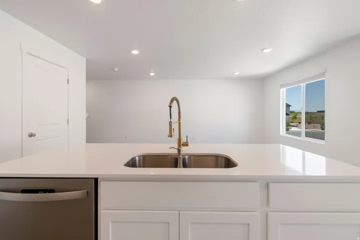 Kitchen island with a double basin stainless steel sink, a gold-toned pull-down faucet, and a light-toned countertop