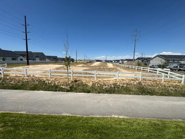 Expansive undeveloped lot featuring a white split-rail fence, a paved pathway, and surrounding residential structures