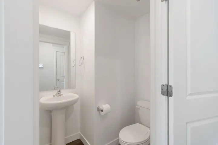 Pedestal sink with chrome faucet, wall-mounted mirror, and wood-finish flooring