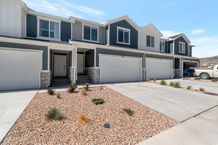 Townhome exterior featuring a multi-tone facade with stone accents, two attached garages, and a gravel xeriscape with minimal plantings