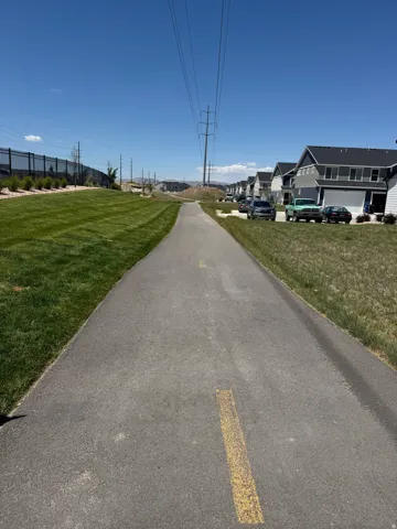 Paved pathway bordered by manicured green space, with suburban residences visible in the background
