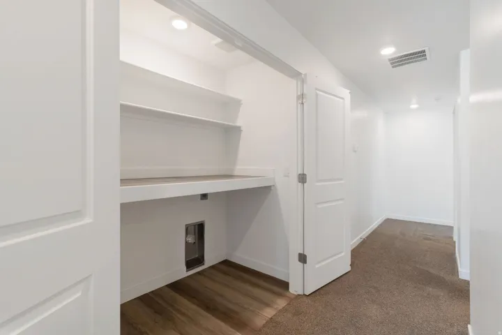 Dedicated laundry area featuring wood-finish flooring, white built-in shelving, and a wood-finish countertop