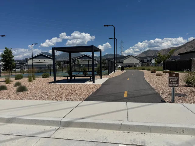 Outdoor amenity area featuring a paved pathway, covered pergola with picnic seating, and tennis courts