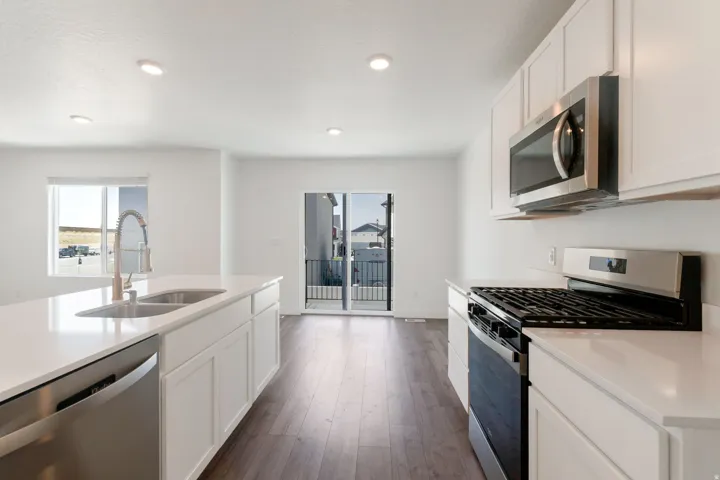 Kitchen featuring white cabinetry, stainless steel appliances, a center island with double sink, light countertops, and wood-finish flooring