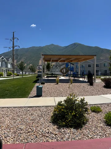 Community park area featuring a covered picnic structure, playground equipment, open green space, and mountain backdrop