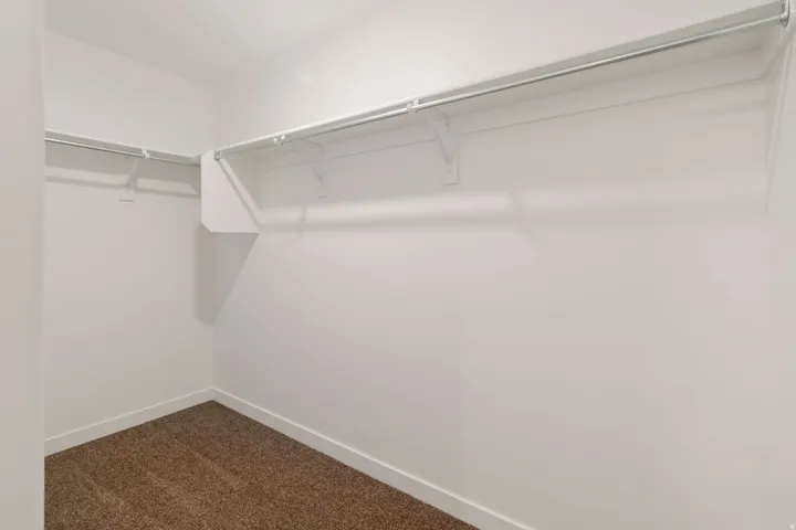 Walk-in closet with white walls and baseboards, featuring brown carpet flooring, and two levels of white wire shelving and hanging rods