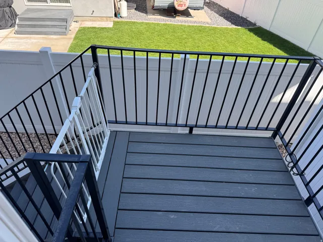 Deck featuring composite decking, black metal railings, and a white vinyl privacy fence