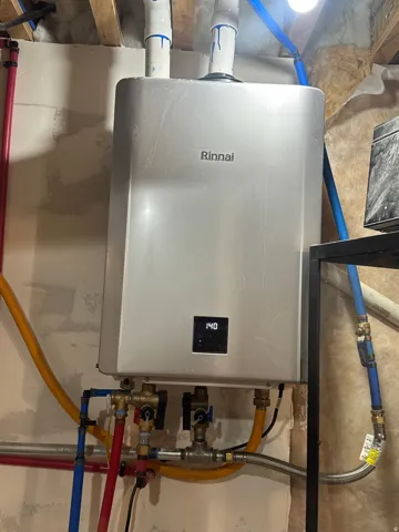 Rinnai tankless water heater with digital display, visible plumbing connections, and associated utility lines