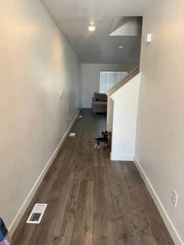 Hallway featuring wood-finish flooring, white baseboards, recessed ceiling lighting, and a partial staircase with a white railing