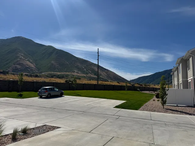 Expansive mountain backdrop with a manicured lawn, concrete parking area, and a privacy fence