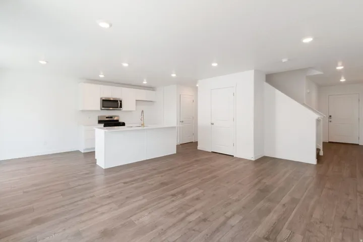 Open-concept living space with wood-finish flooring, recessed lighting, a modern white kitchen island with an integrated sink, white cabinetry, and stainless steel appliances