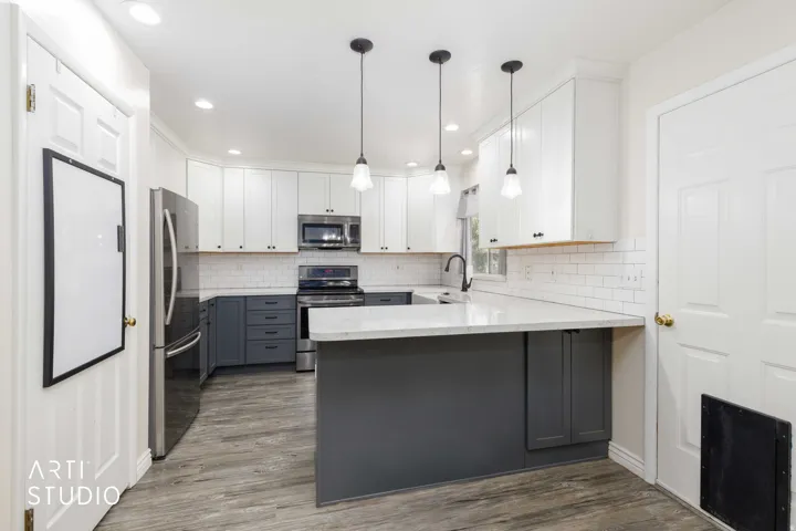 Modern kitchen featuring two-tone cabinetry, stainless steel appliances, wood-finish flooring, white subway tile backsplash, and a central island with a solid surface countertop