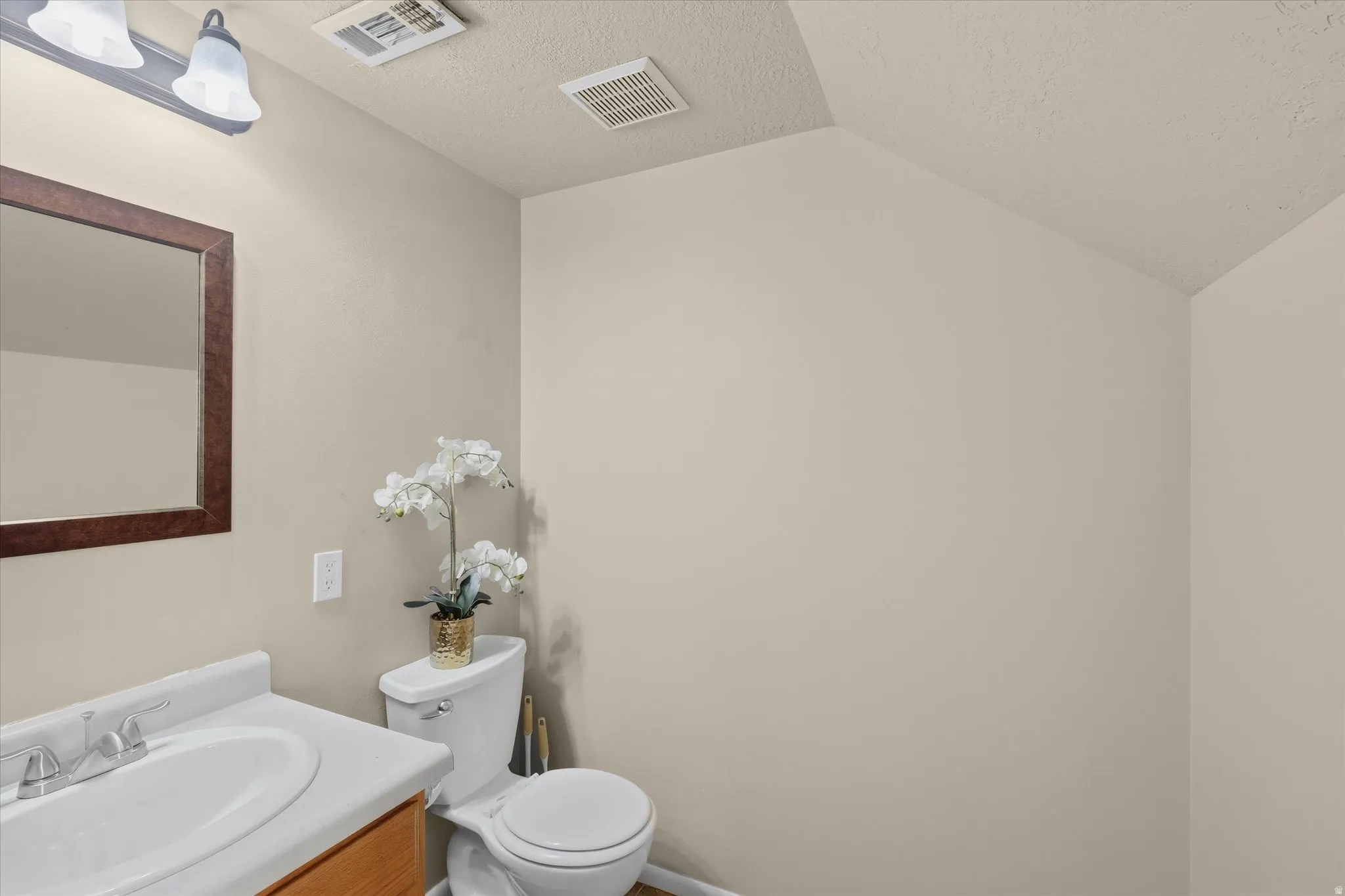 Bathroom featuring a single vanity with a white countertop and wood-finish cabinetry, a framed wall mirror, and a two-bulb vanity light fixture