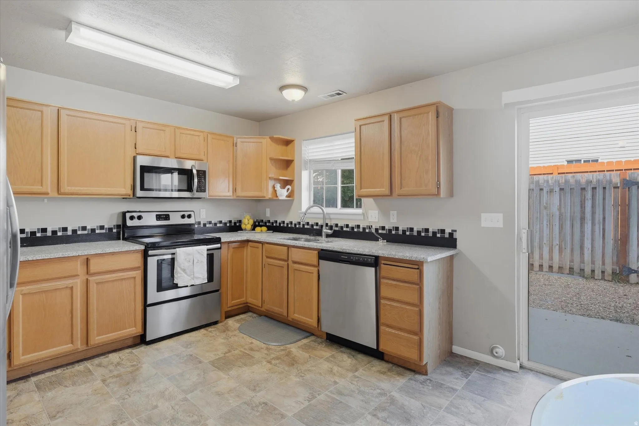 Kitchen featuring wood cabinetry, stainless steel appliances, speckled countertops, and a black and white tile backsplash
