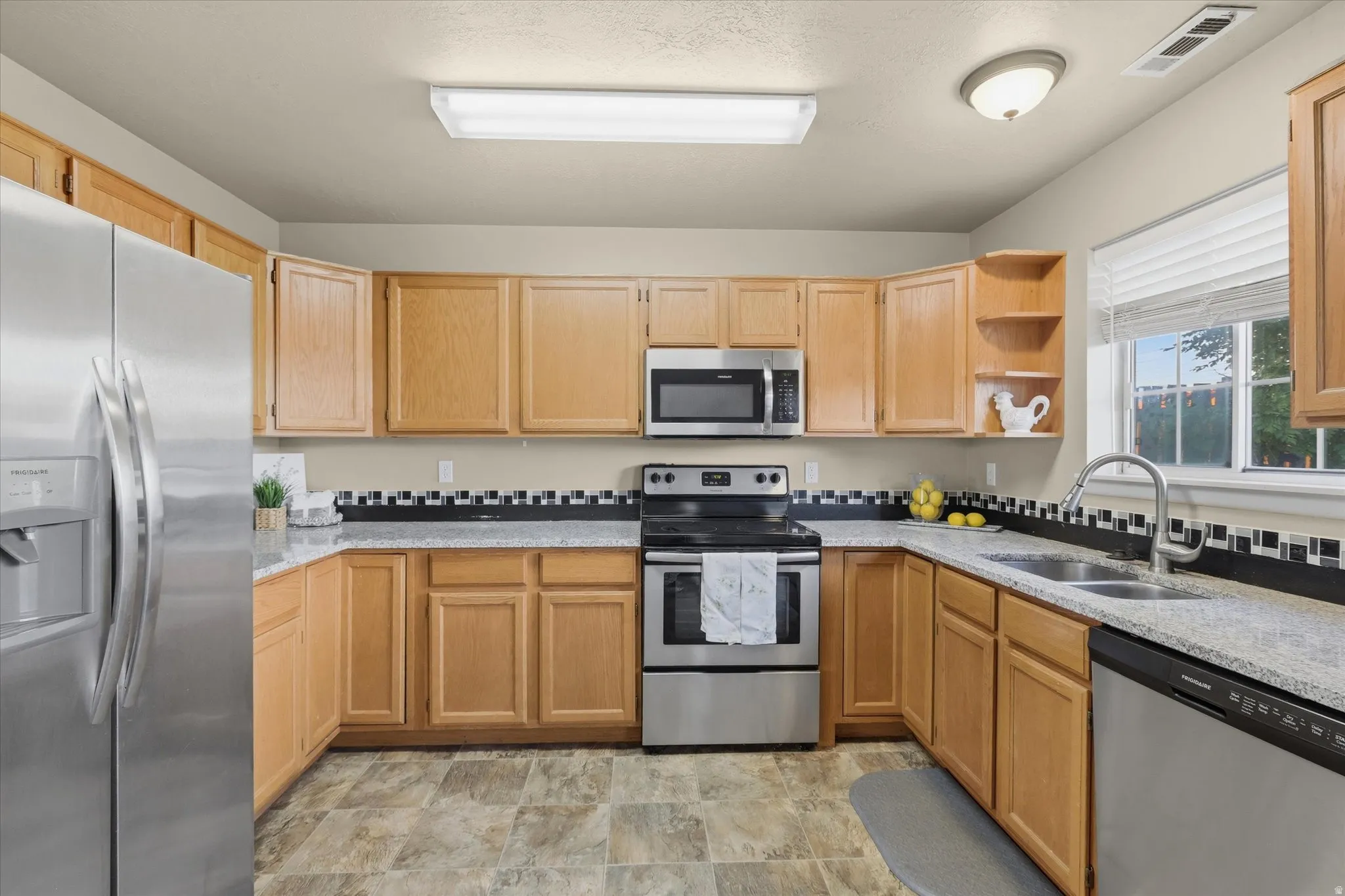 U-shaped kitchen featuring light wood cabinetry, stone-finish countertops, stainless steel appliances, and a tiled backsplash