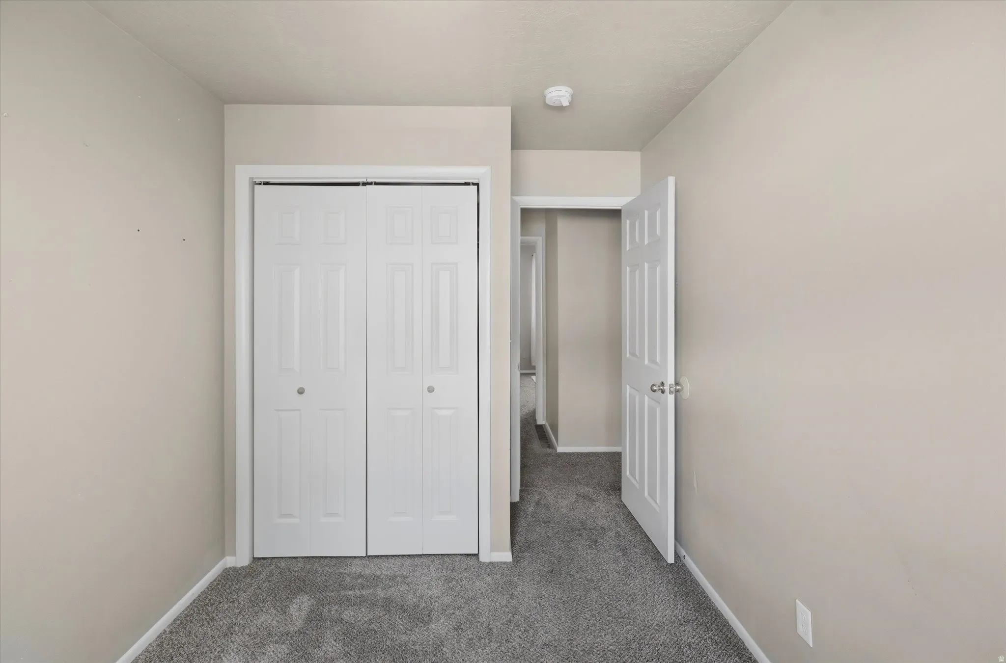 Room featuring neutral painted walls, gray carpet flooring, and a white bi-fold closet door