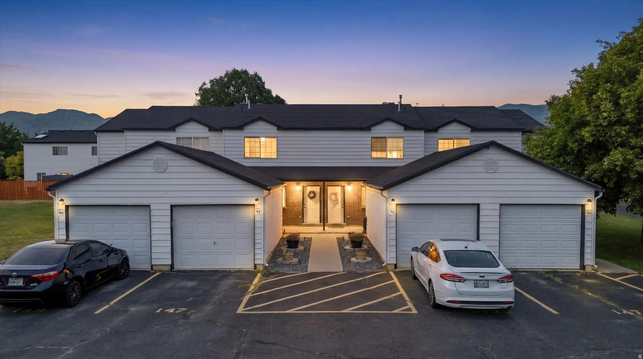 Two-story multi-unit structure with a black shingled roof, white horizontal siding, and integrated garages