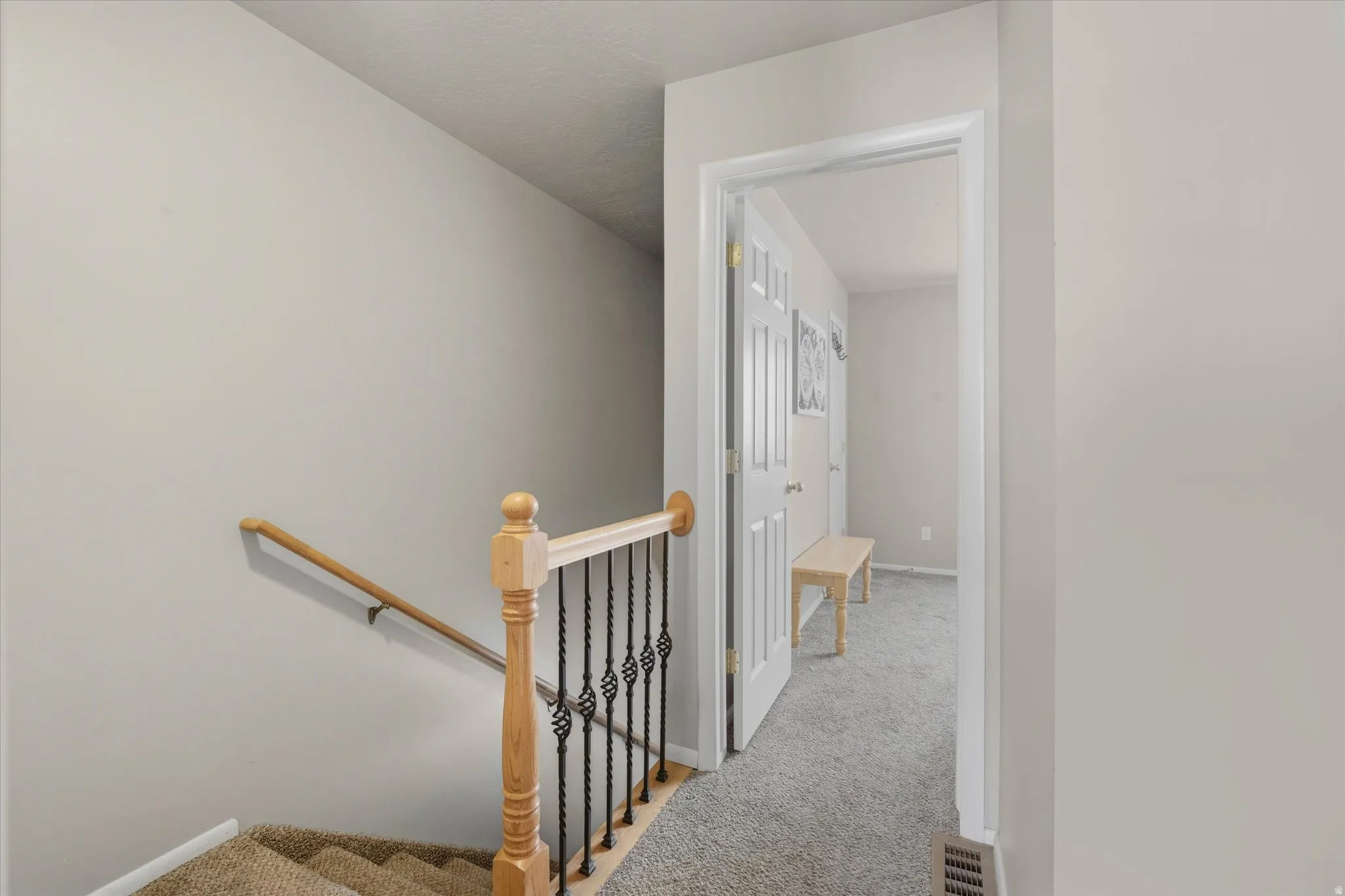 Carpeted staircase with a light wood handrail and wrought iron balusters