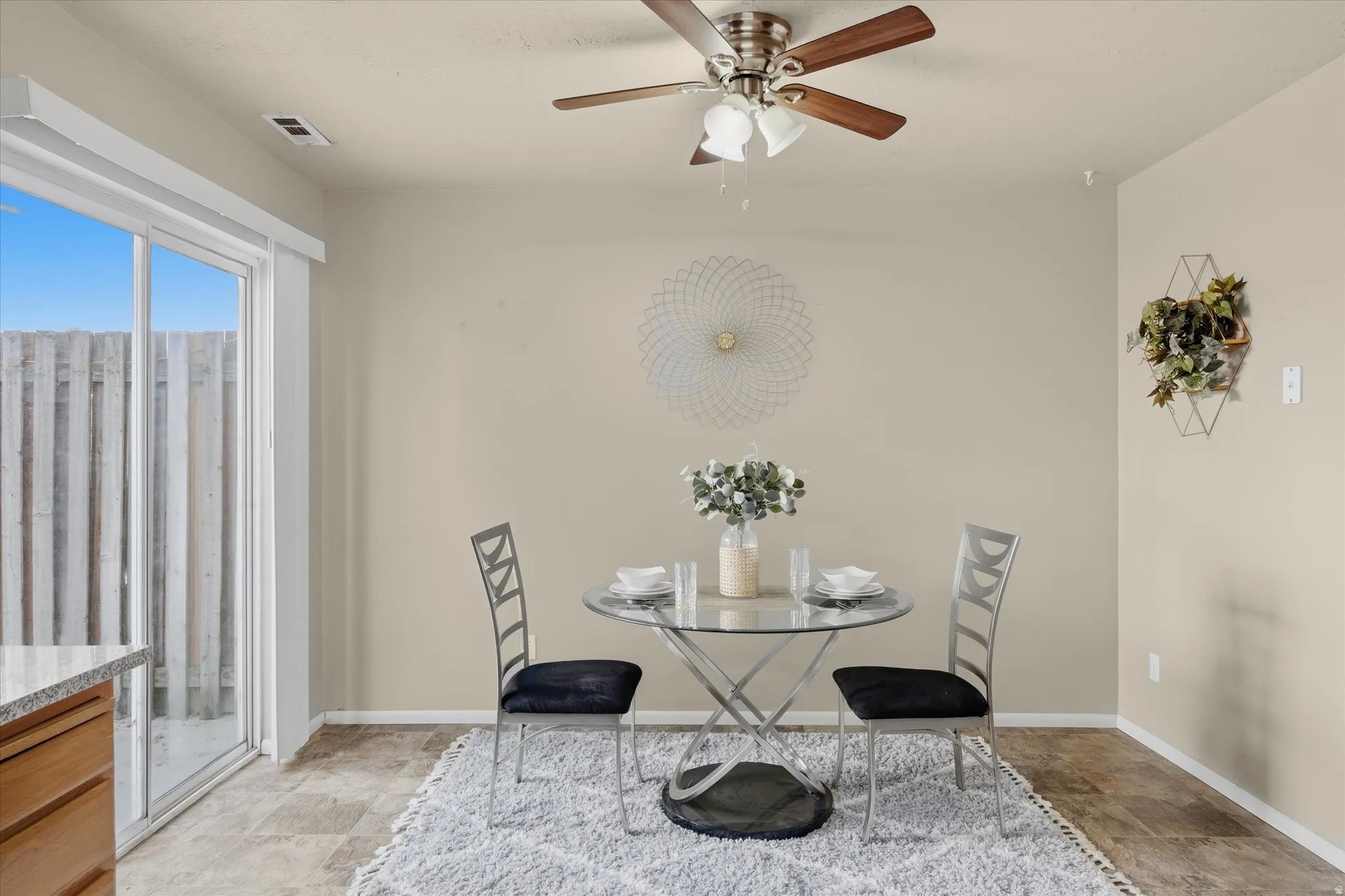 Dining area featuring a ceiling fan with integrated lighting, patio door with vertical blind, and neutral wall tones