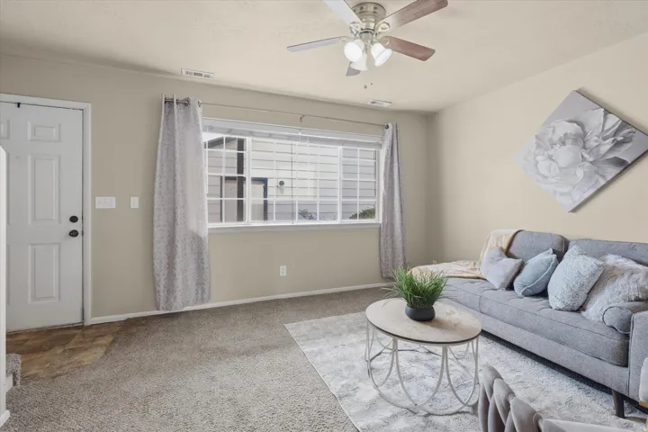 Living space featuring neutral wall paint, a ceiling fan with integrated lighting, and a large window with horizontal blinds