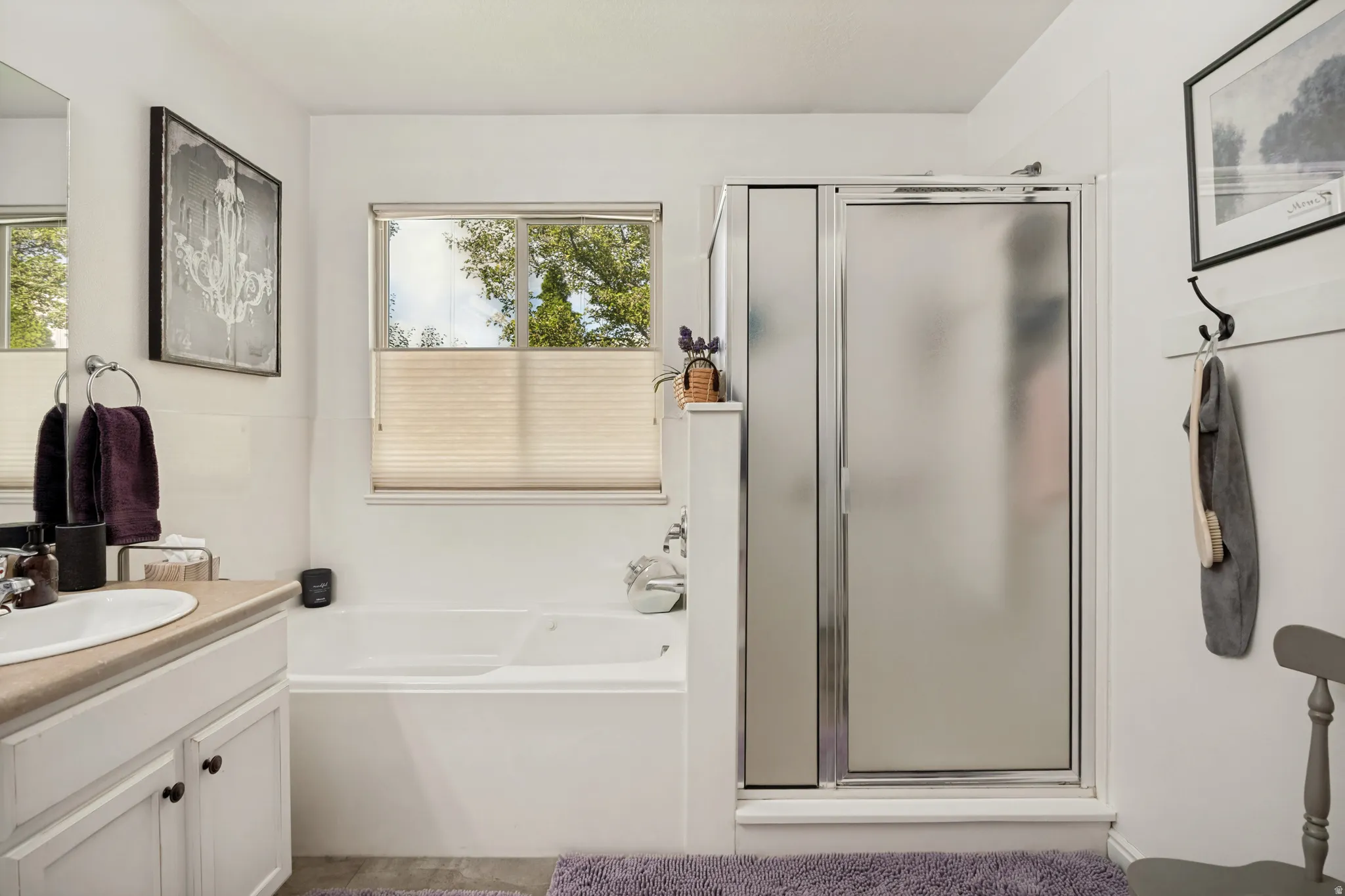 Bathroom featuring a built-in tub, a separate shower with a frosted glass enclosure, a single vanity with a white basin, and a window with blinds