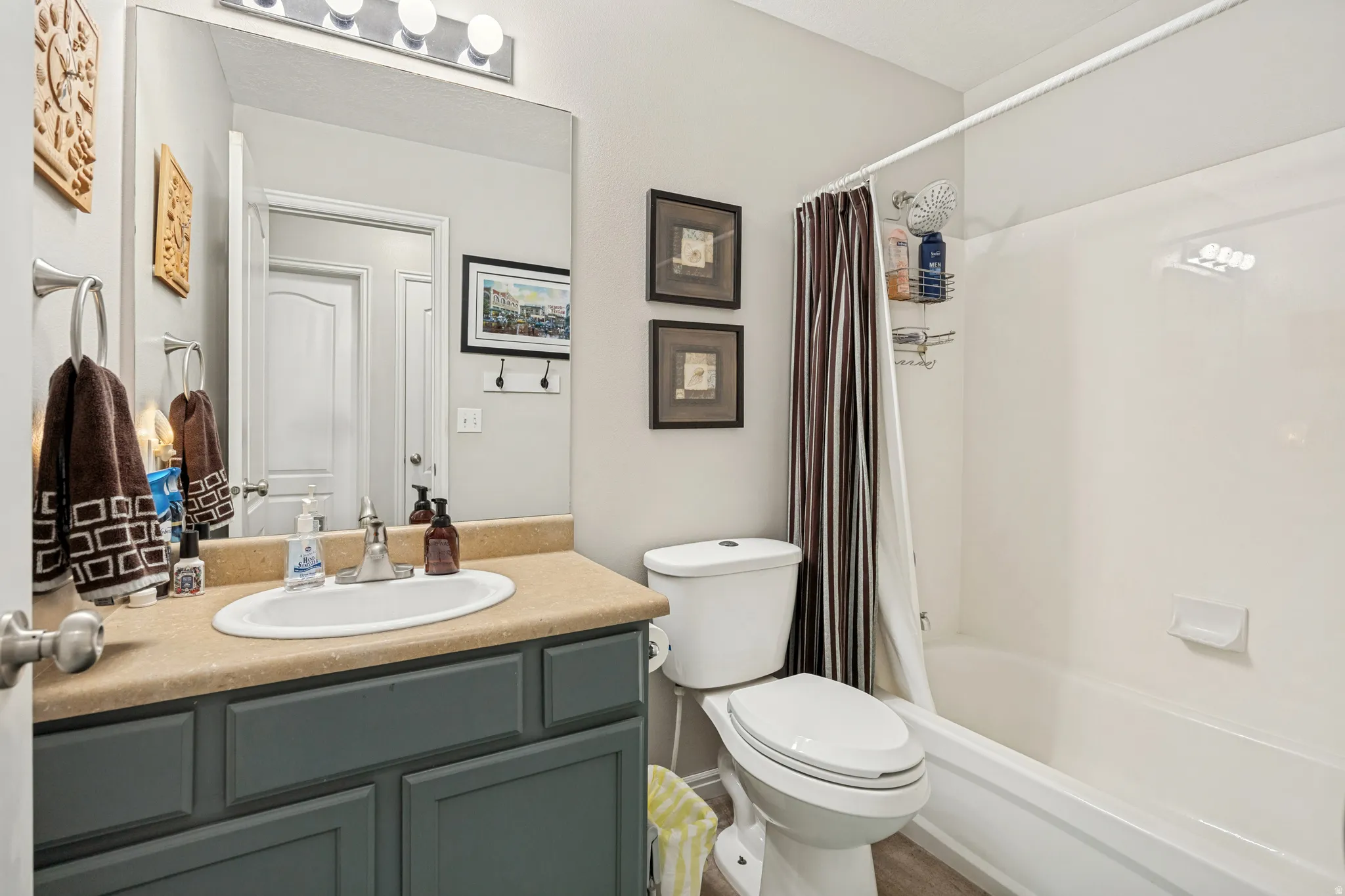 Bathroom featuring a vanity with a light-toned countertop and dark cabinetry, a built-in sink with a chrome faucet, a large wall-mounted mirror, and a white bathtub with a shower