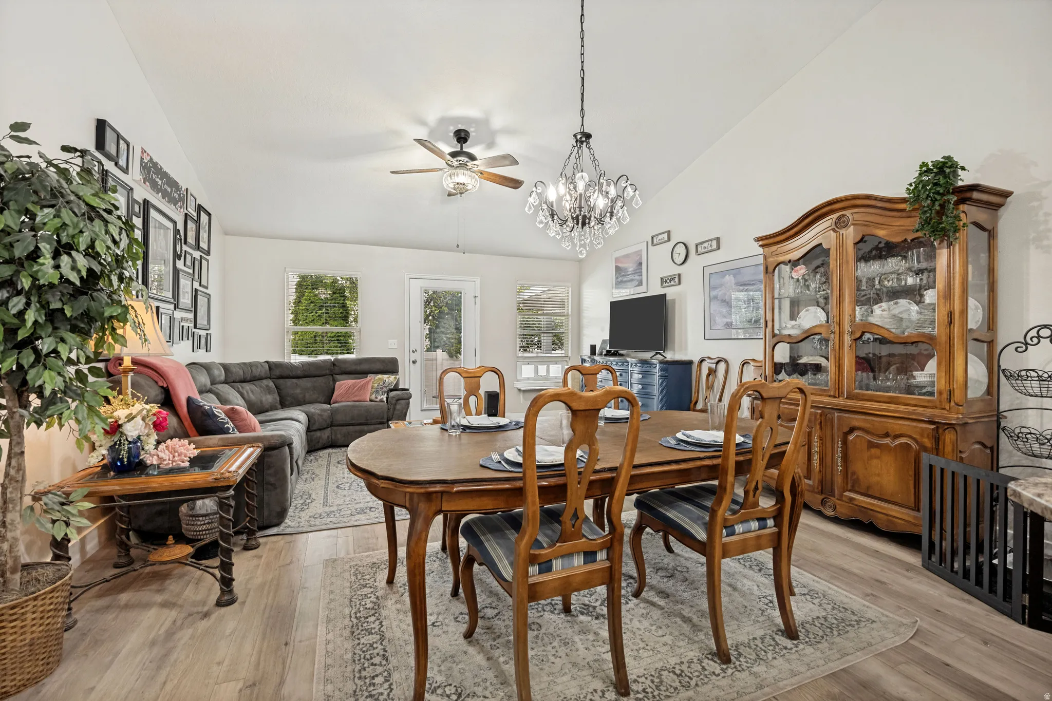 Vaulted ceiling living and dining area featuring wood-finish flooring, a crystal chandelier, recessed lighting, and multiple windows