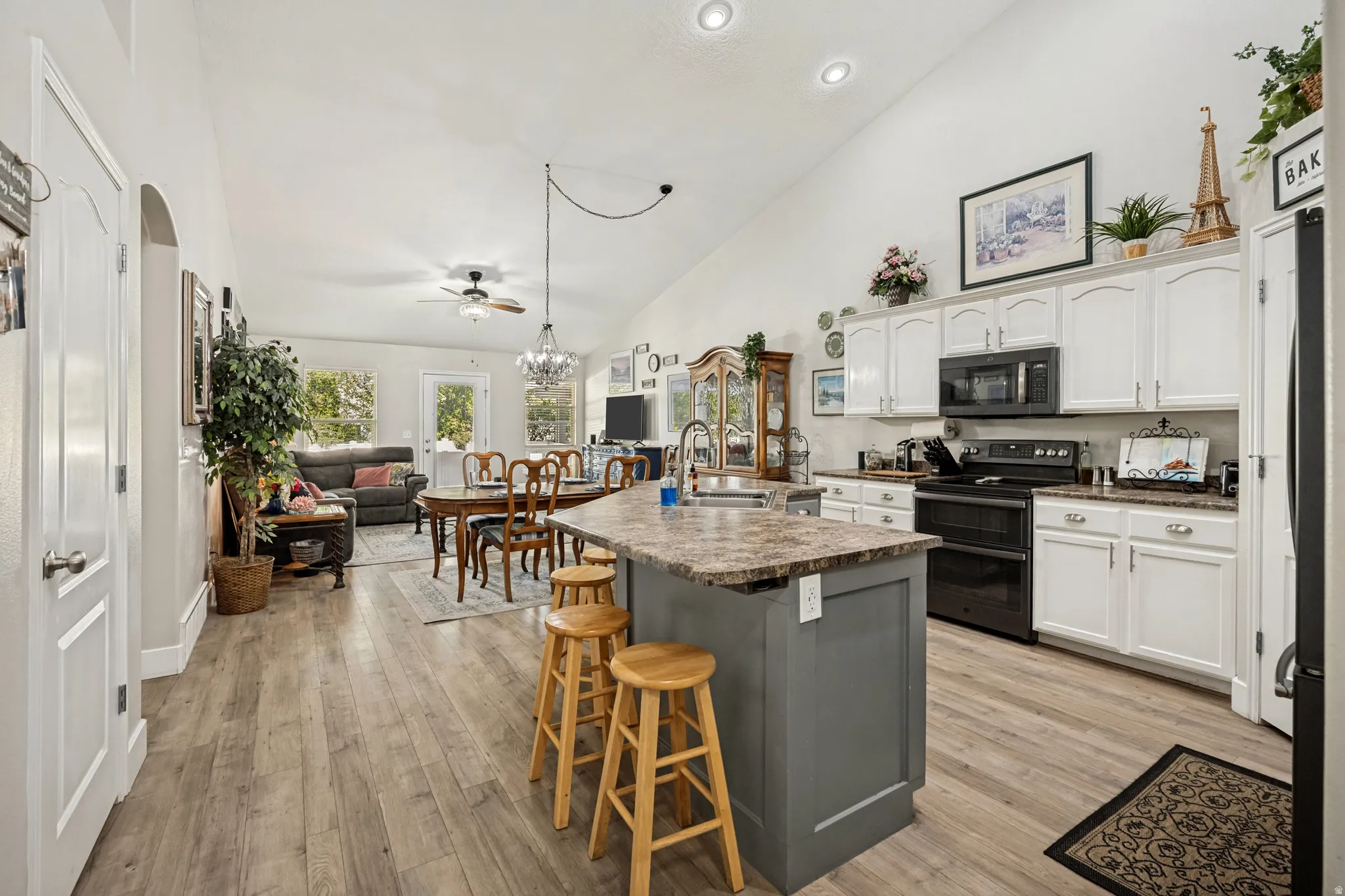 Open-concept kitchen and living area featuring wood-finish flooring, vaulted ceilings, recessed lighting, and a kitchen island with seating