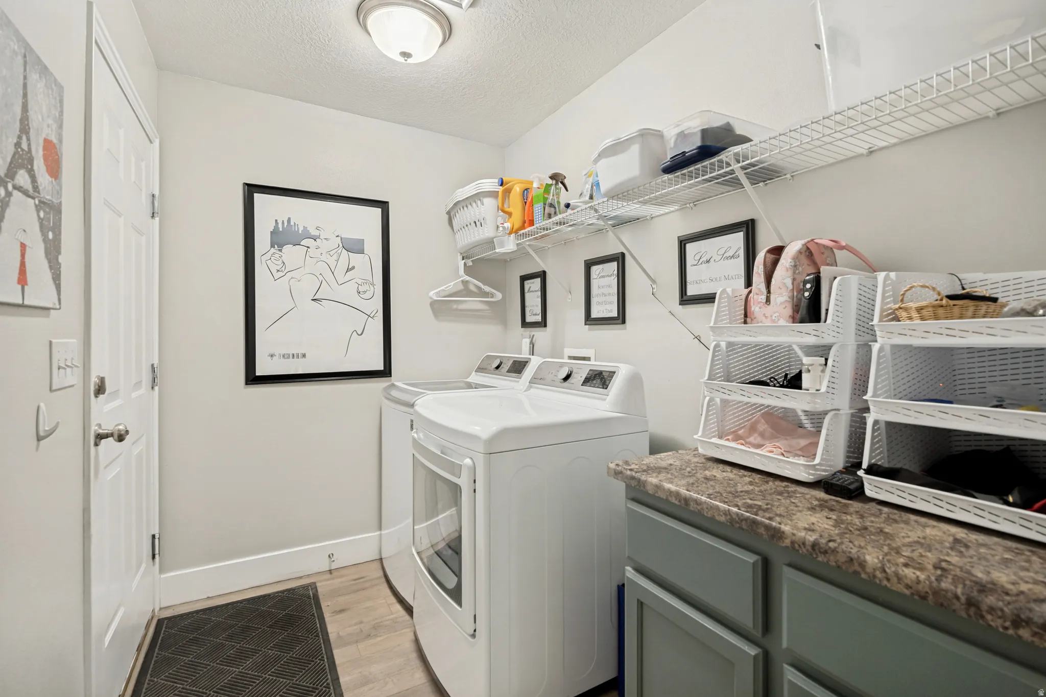 Dedicated laundry room featuring wood-finish flooring, a contemporary ceiling light fixture, and a built-in countertop with cabinet storage