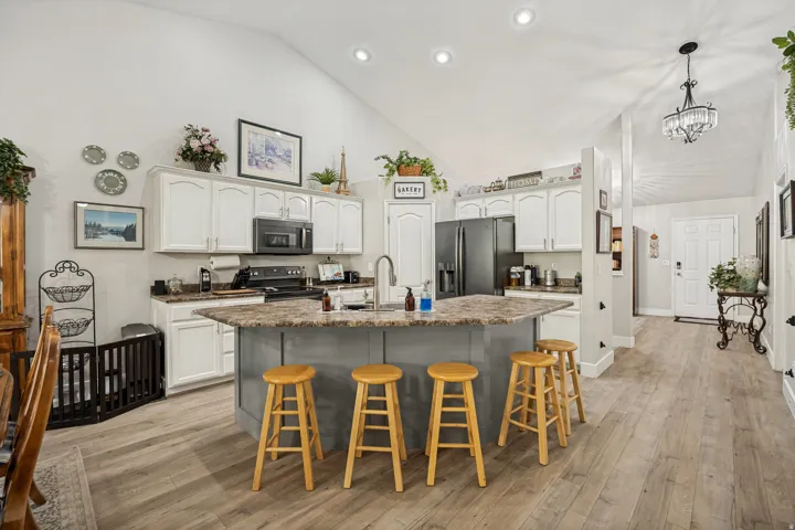 Kitchen featuring wood-finish flooring, vaulted ceilings with recessed lighting, white cabinetry, and dark countertops