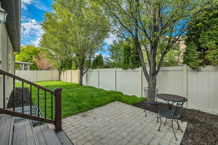 Private backyard featuring a paver patio, lush green lawn, mature trees, and a perimeter privacy fence