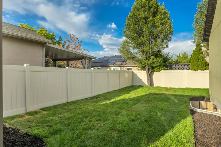 Private side-yard space featuring a verdant lawn, full perimeter fencing, and established tree